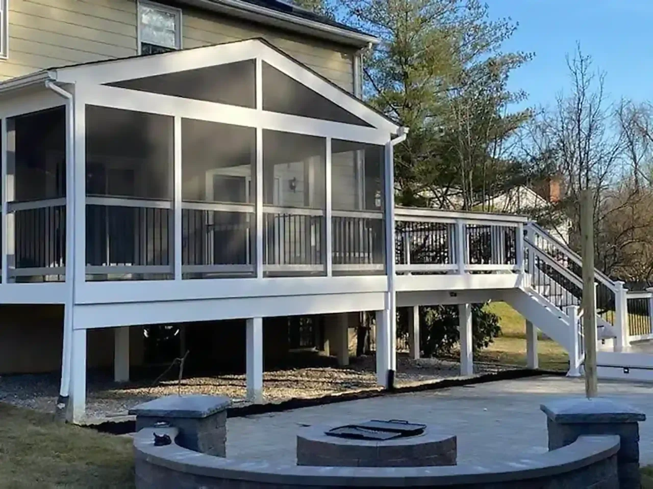 Photo of a screened-in, covered deck that is raised with a patio and fire pit and built-in seating