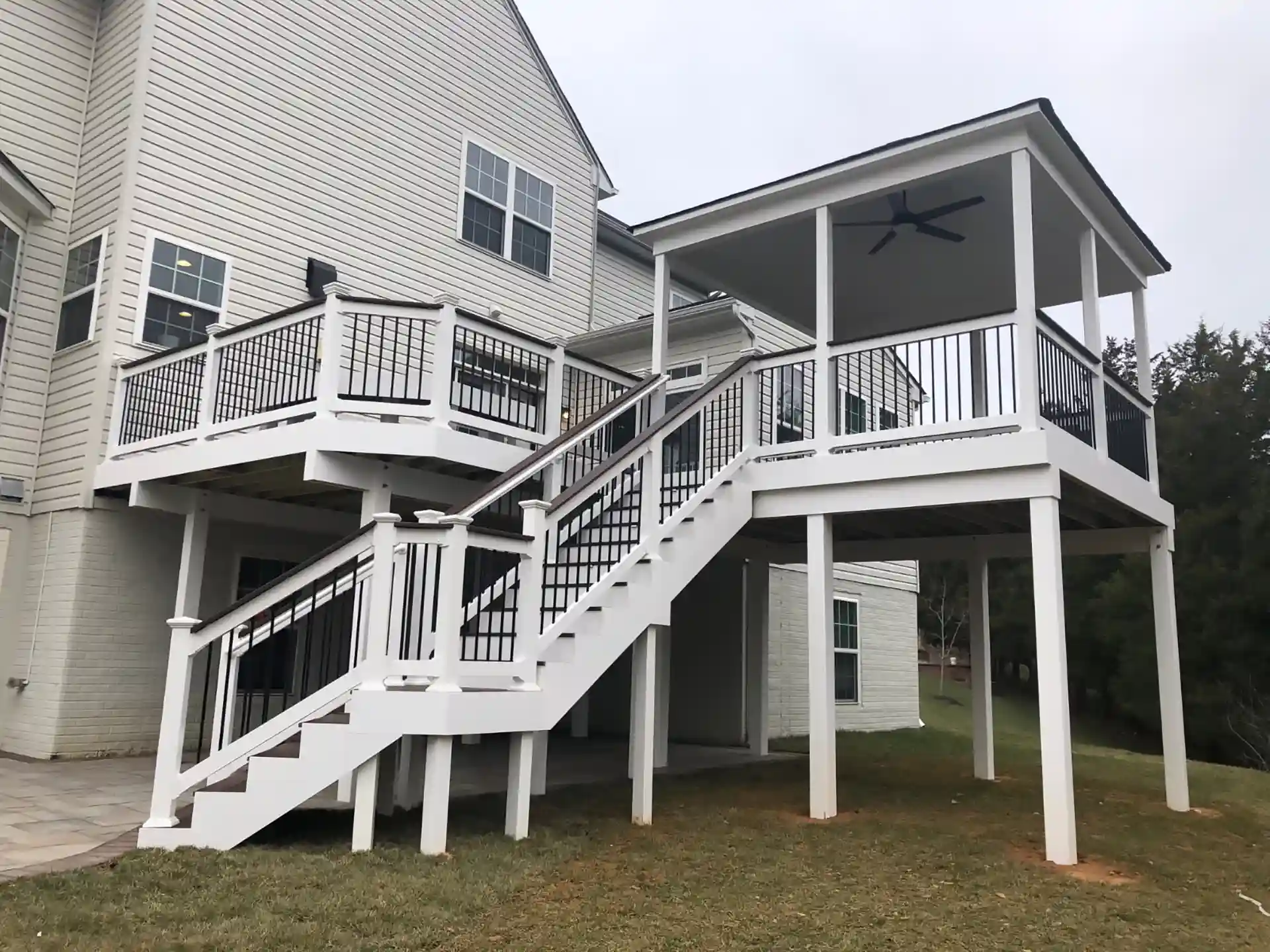 Photo of two-level white and brown deck with covered area, black railings, and stairs. Deck is made with Trex Decking.
