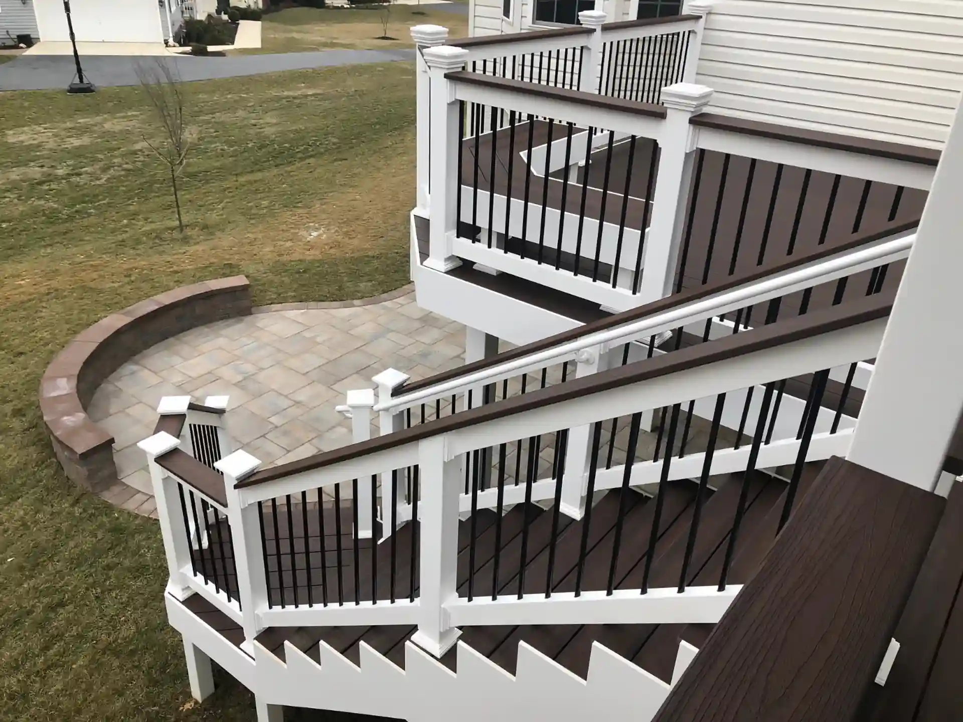 Photo of multi-tiered deck stairs leading to circular paver patio with curved retaining wall.
